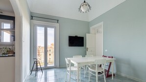 A dining area with a white table and chairs, a television mounted on the wall, and a sliding glass door leading to an outdoor balcony. - Casa Garibaldi in Piazza by Wonderful Italy (Palermo)