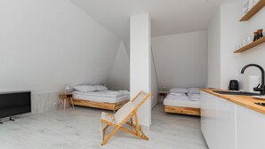 Habitación moderna y minimalista con dos camas de madera, una hamaca, un televisor de pantalla plana y una pequeña cocina.