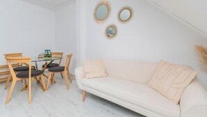 Una sala de estar moderna con una mesa de comedor de vidrio, sillas de madera, un sofá color beige y tres espejos colgados en la pared.
