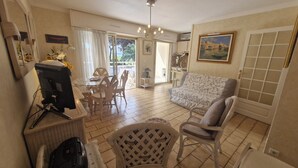A spacious living room with a dining area, a television, and a wicker chair. - STUDIO + SLEEPING AREA CLOSE TO SHOPS AND BEACHES (Sainte-Maxime)