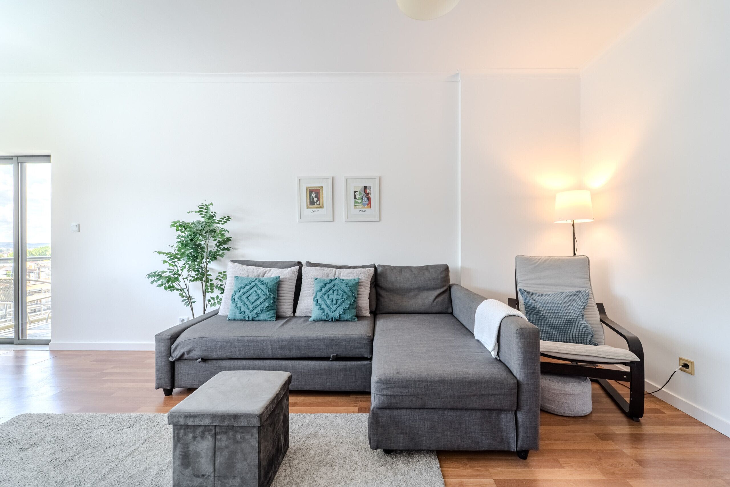 A modern living room with a grey sectional sofa, a small round table, a floor lamp, and a potted plant.