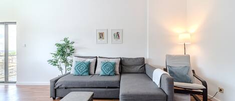 A modern living room with a grey sectional sofa, a small round table, a floor lamp, and a potted plant.