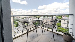 Un balcón con dos sillas y una mesa, con vista a un paisaje urbano con edificios y cielo despejado.