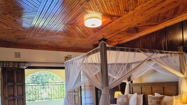 A bedroom with a four-poster bed, wooden ceiling, and a view of greenery outside. - A  farmhouse on the Tea farm estate (Kiambu County)