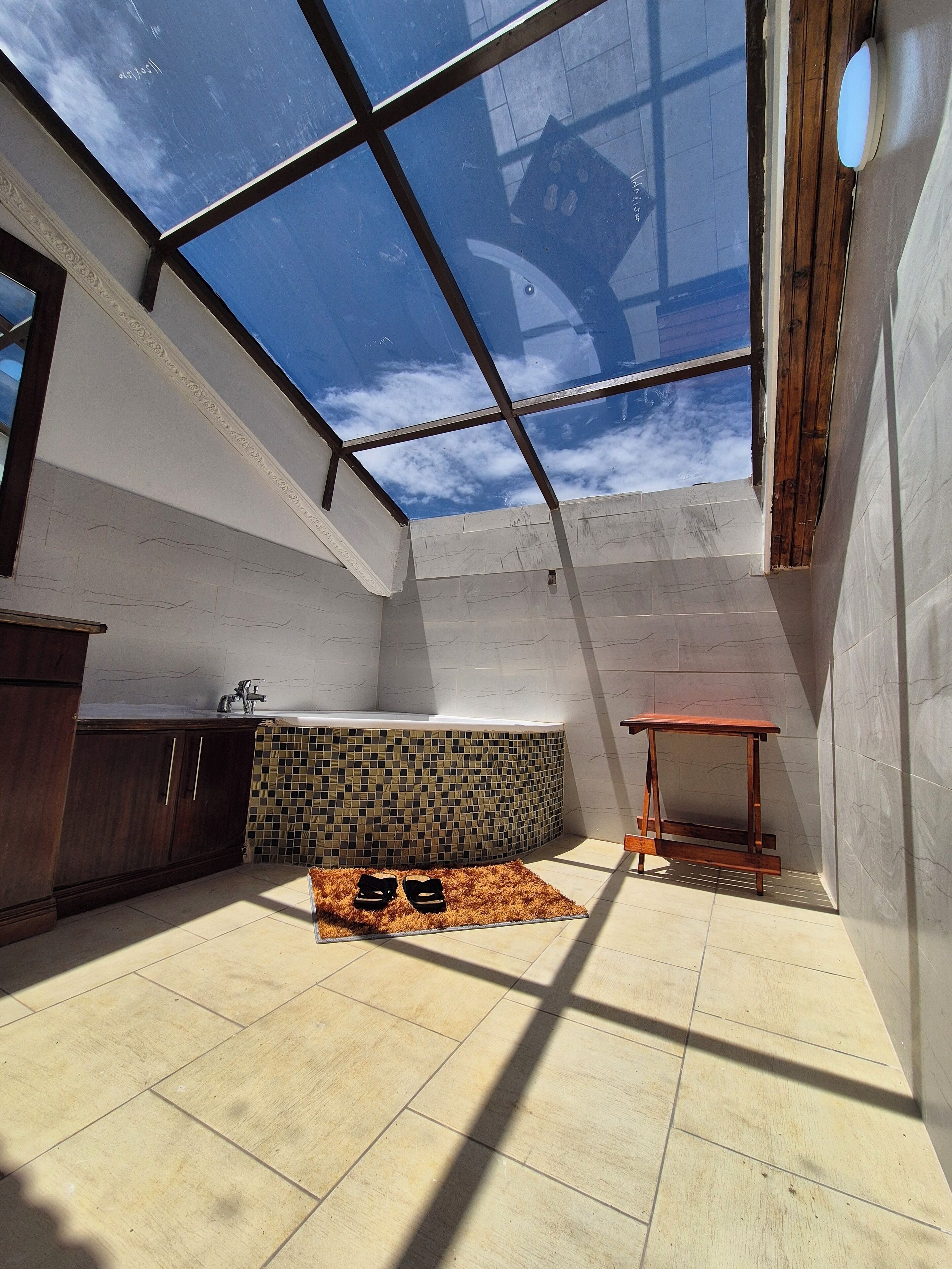 A high-ceilinged room with a skylight, a tiled backsplash, a wooden table, and a pair of shoes on a rug. - A  farmhouse on the Tea farm estate (Kiambu County)