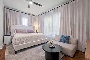 A modern bedroom with a bed, a sofa, a small table, and a ceiling fan.