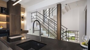 Eine moderne Küche mit schwarzem Arbeitsplatz, Edelstahl-Spüle und Holzschränken. Eine Treppe mit schwarzen Geländern führt in einen Außenbereich.