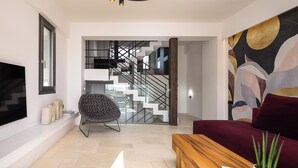 Ein modernes Wohnzimmer mit einer Couch, einem Couchtisch aus Holz, einem Sessel, einem Fernseher und einer Treppe, die zu einer oberen Etage führt.