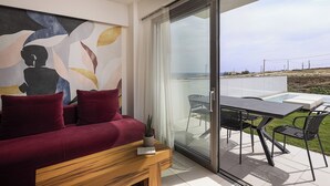 Ein modernes Wohnzimmer mit einem roten Sofa, einem Holztisch und einer Glastür, die auf eine Außenpatio mit Pool und Stühlen führt.