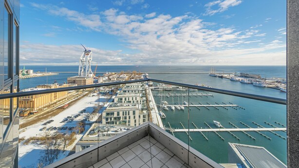 Een balkon op een hoog gebouw met uitzicht op een jachthaven, boten en een verre brug.