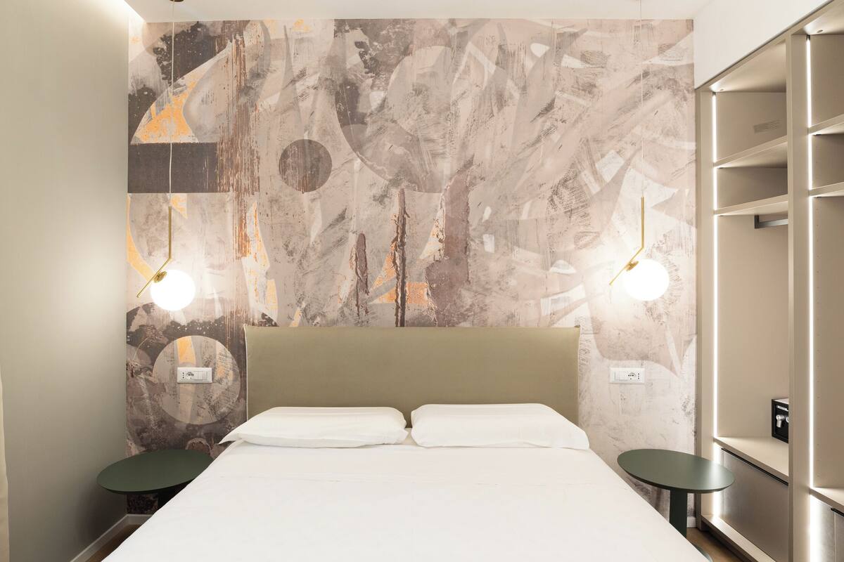 Moderni hotellihuone, jossa on suuri sänky, kaksi yöpöytää ja seinä, jossa on abstraktia taidetta.