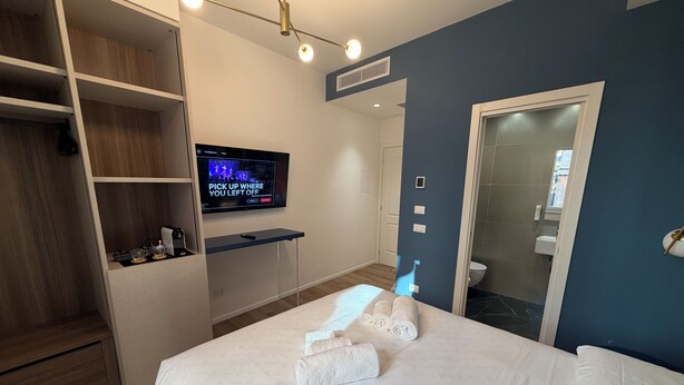 Ein modernes Hotelzimmer mit Bett, Fernseher, Kleiderschrank und Badezimmer.