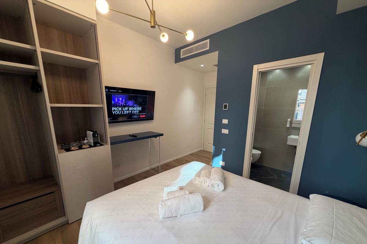 Moderni hotellihuone, jossa on sänky, televisio, vaatekaappi ja kylpyhuone.