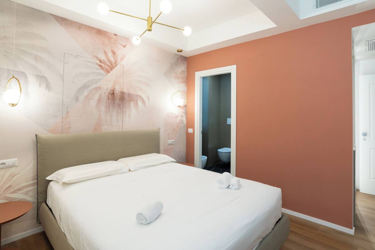Hotellihuone, jossa on sänky, pyöreä peili ja kylpyhuone, joka näkyy avoimesta ovesta.