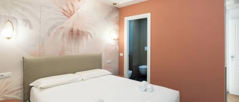 A hotel room with a bed, a round mirror, and a bathroom visible through an open door.