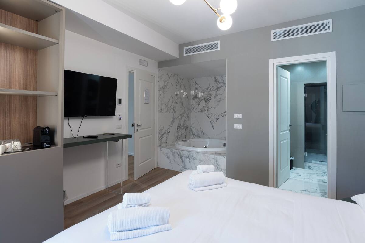 Moderni hotellihuone, jossa on suuri sänky, marmoriseinäinen kylpyhuone ja seinälle asennettu taulutelevisio.