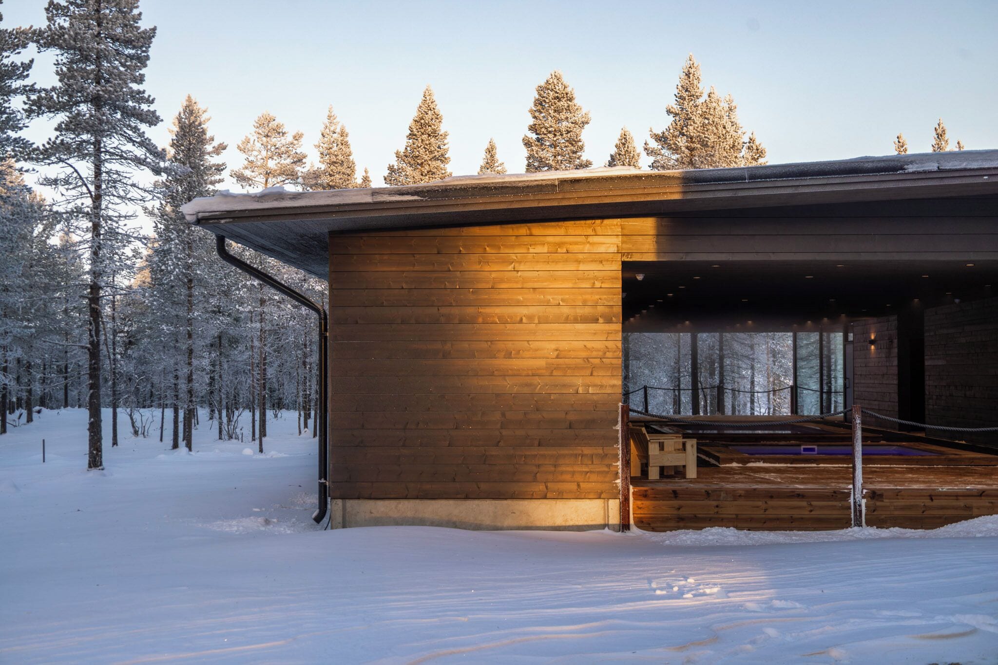 A wooden cabin with a covered porch, surrounded by a snowy forest.