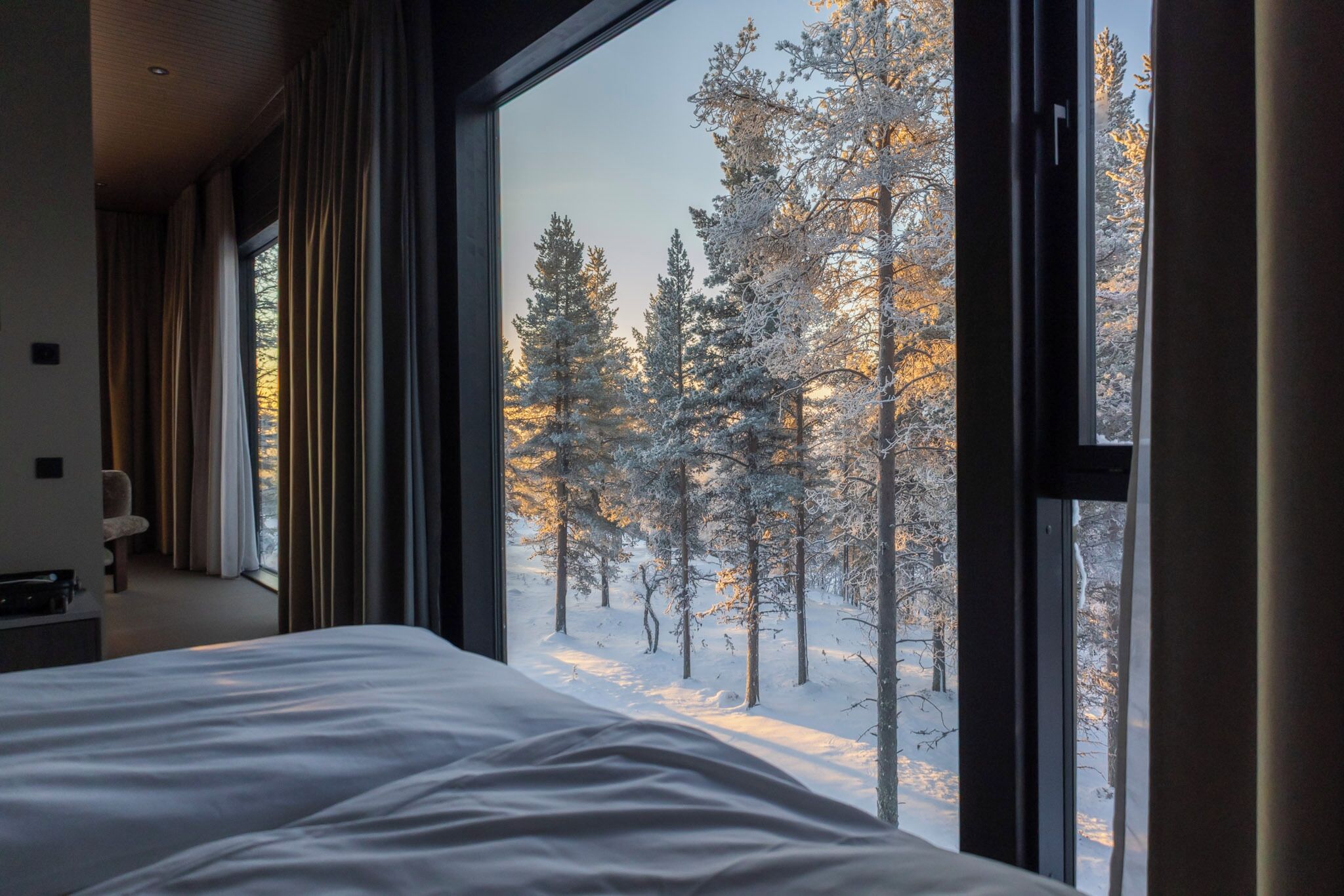 A bedroom with a large window overlooking a snowy forest.