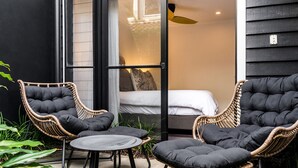 A room with a bed, two wicker chairs, a small table, and a ceiling fan.