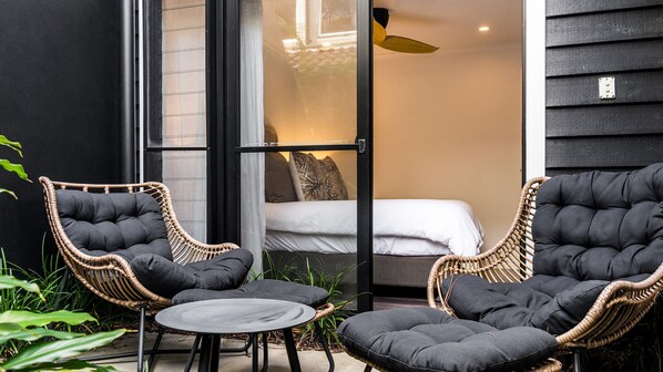 A room with a bed, two wicker chairs, a small table, and a ceiling fan.