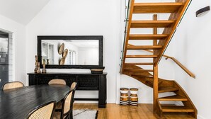 A modern interior with a dining area, a black-framed mirror, a wooden staircase, and a minimalist design.