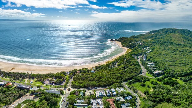 An aerial view of a coastal area with a beach, residential buildings, and a lighthouse.