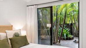 A bedroom with a large sliding glass door leading to a tropical garden.