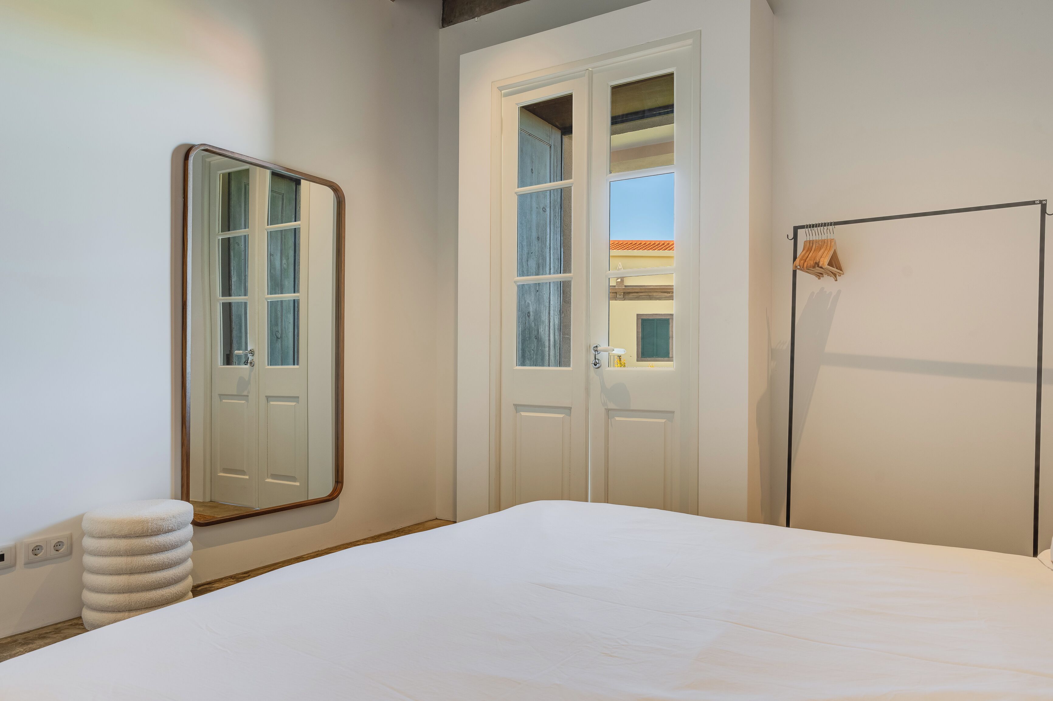 A bedroom with a bed, a large mirror, two doors, and a hanging rack.