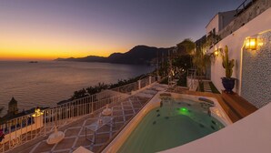 Terraza en la azotea con hidromasaje, con vista a un cuerpo de agua y montañas al atardecer.