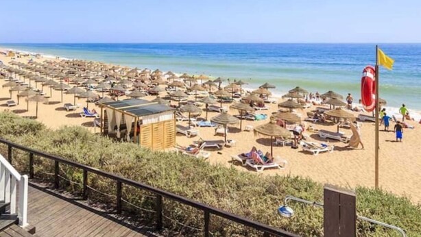 A beach with numerous sun umbrellas and lounge chairs, a wooden deck, and a lifebuoy on the shore. - 2 bed renovated apartment in vale do lobo Algarve (Loulé)