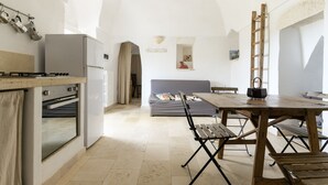 A kitchen with a stove, oven, and refrigerator. There is a dining table with benches and a ladder leaning against the wall. - Dimora Upupa by Wonderful Italy (Ostuni)