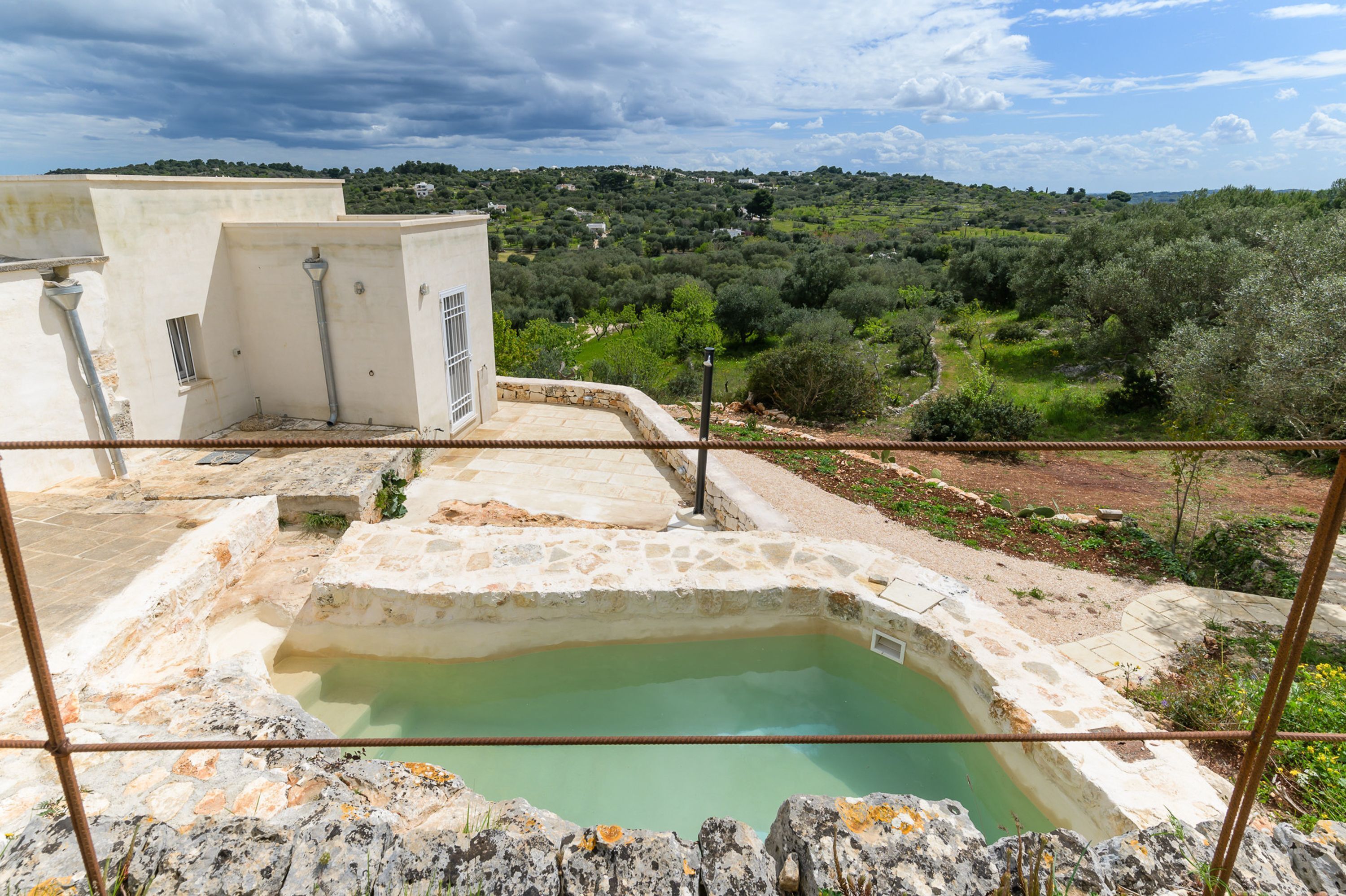 A rooftop pool with a stone edge and a view of a green landscape.