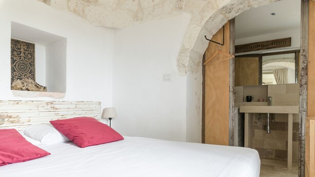 A bedroom with a bed, a nightstand, a mirror, and a bathroom visible through an archway. - Dimora Upupa by Wonderful Italy (Ostuni)