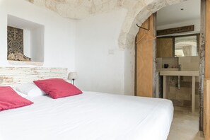 A bedroom with a bed, a nightstand, a mirror, and a bathroom visible through an archway. - Dimora Upupa by Wonderful Italy (Ostuni)