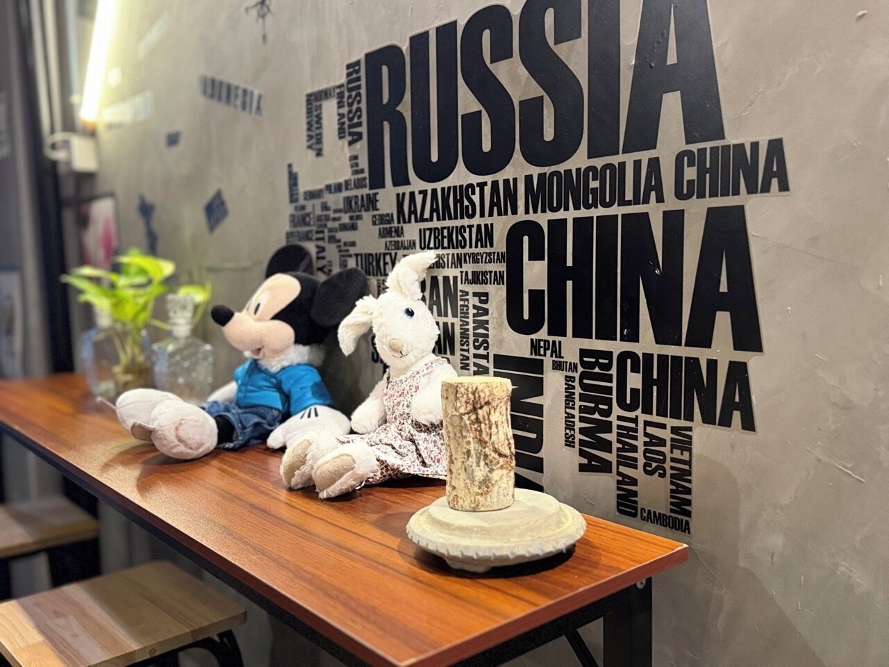 A table with two plush toys and a decorative item against a wall with country names.