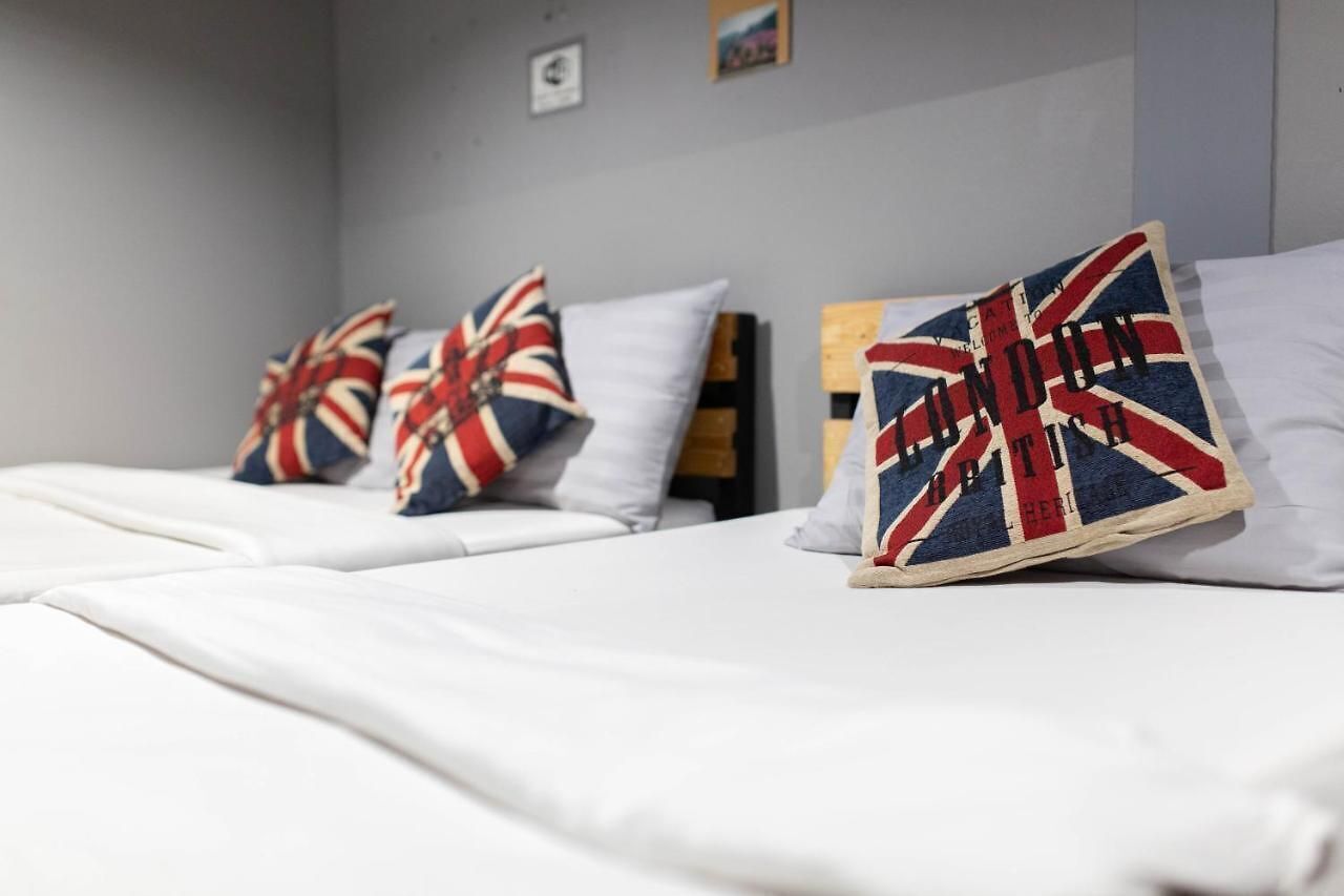 Une chambre d’hôtel avec trois lits, chacun agrémenté d’un oreiller orné d’un motif représentant l’Union Jack.