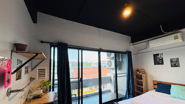 Une chambre moderne dotée d’une grande porte-fenêtre coulissante, d’un lit, d’un bureau avec une chaise et d’une petite étagère.