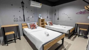 Une chambre avec deux lits simples, chacun doté d’une tête de lit en bois et de linge de lit blanc. On y trouve deux petites tables en bois, une de chaque côté des lits. Les murs sont décorés de divers motifs, notamment un lampadaire, des oiseaux et des ampoules.
