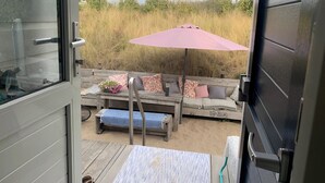 An open door to a deck area with a wooden bench, a small table with a flower arrangement, and a pink umbrella. - Beach house on the North Sea coast - IJmuiden Kleine Strand (IJmuiden)