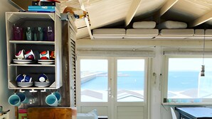 A compact kitchen with a built-in shelf holding dishes and cookware, a wooden table, and a view of the sea through a door. - Beach house on the North Sea coast - IJmuiden Kleine Strand (IJmuiden)