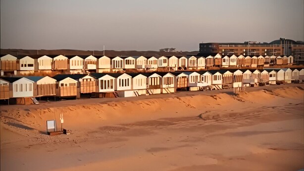A beach with rows of beach huts and a building in the background. - Beach house on the North Sea coast - IJmuiden Kleine Strand (IJmuiden)