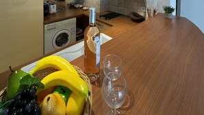A modern kitchen with a built-in oven, microwave, and washing machine, a wooden dining table with a bottle of wine and glasses, and a fruit basket. - HAN1913 (Cannes)