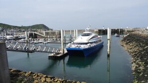 A ferry docked at a pier with a bridge and a rocky shoreline in the background.