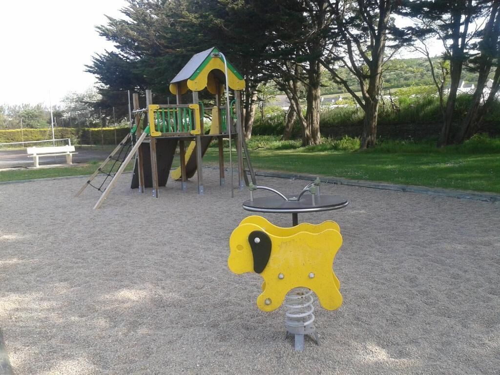 Une aire de jeux avec une balançoire jaune en forme d’animal et une structure d’escalade verte.