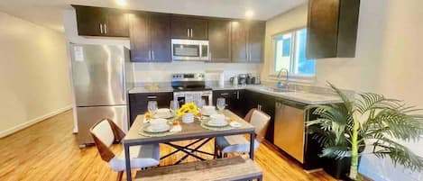 Enjoy meals in this stylish kitchen and dining area, featuring a dishwasher, stainless steel appliances, and a wooden table for four.