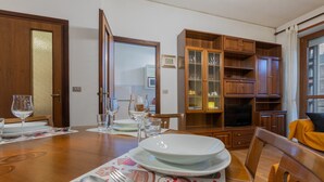 A dining area with a wooden table set for four, a television in the background, and a wooden cabinet with glass doors.