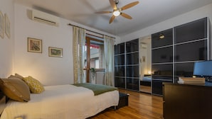 A bedroom with a bed, a desk, a chair, a ceiling fan, and a window with curtains.