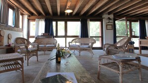 A spacious room with wicker furniture, wooden beams, large windows, and a table with a bottle and glasses. - Venice Photobirding Nature And Culture (Mestre)