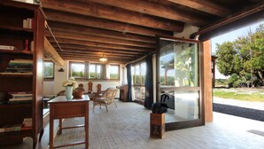 A cozy room with a wooden ceiling, a dining table with chairs, a bookshelf, and a large window offering a view of greenery outside. - Venice Photobirding Nature And Culture (Mestre)