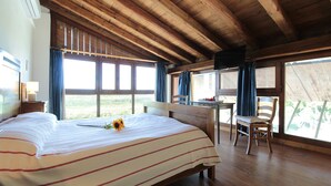 A bedroom with a large bed, a wooden desk, and a chair. There are windows with curtains, a wooden ceiling, and a view of the outdoors. - Venice Photobirding Nature And Culture (Mestre)
